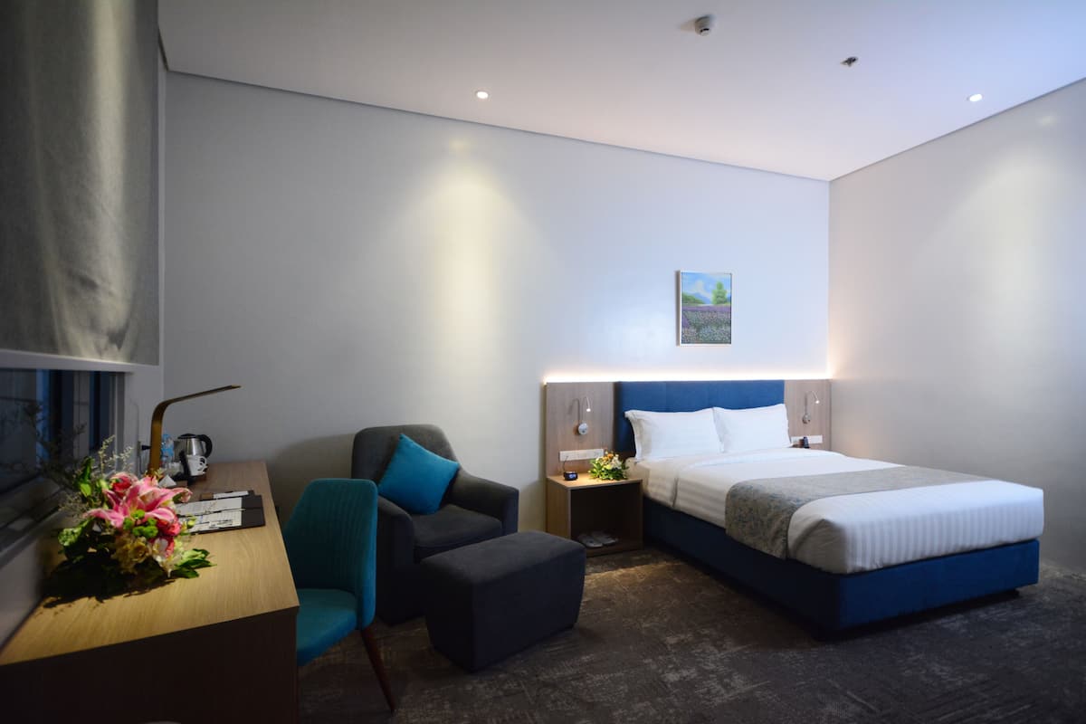 A modern hotel room with a bed, a desk, a chair, and a nightstand.