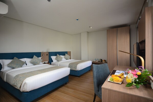 A hotel room with two beds, a desk with a chair, and a small table with a fruit plate and flowers. - Blue Lotus Hotel Davao (Davao)