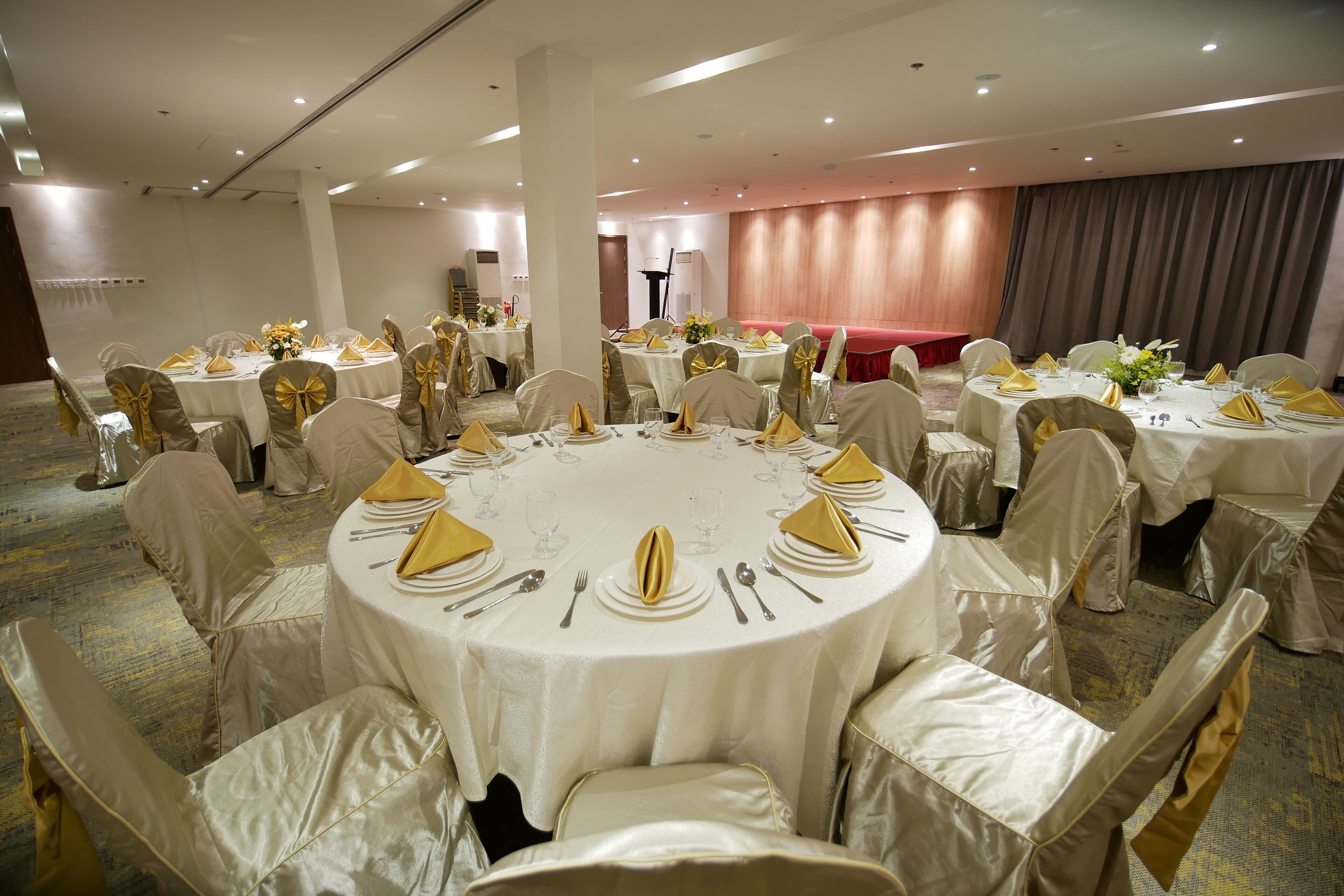 Een balzaal met ronde tafels, gedekt voor een formeel evenement, met witte tafelkleden en gouden servetten.