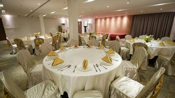 Een balzaal met ronde tafels, gedekt voor een formeel evenement, met witte tafelkleden en gouden servetten.