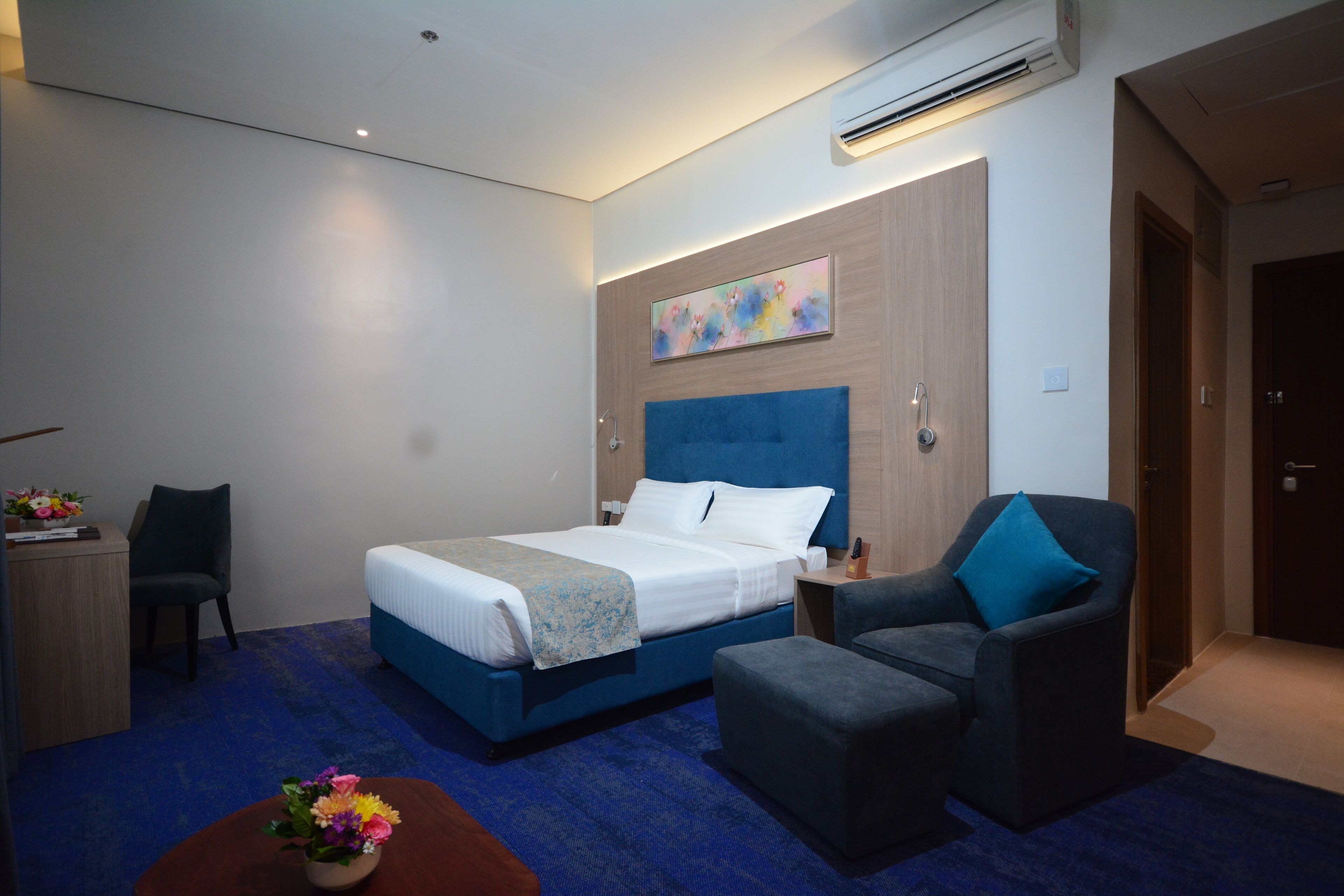 A hotel room with a bed, a desk, a chair, and a small table with flowers.