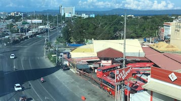 A wide road with vehicles, a red building labeled "TILE DEPOT," and a mountainous landscape in the background.