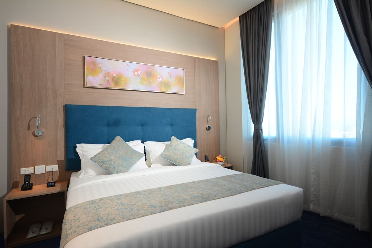 A hotel room with a large bed, a headboard, a bedside table with a phone, and a painting on the wall.