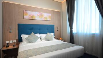 A hotel room with a large bed, a headboard, a bedside table with a phone, and a painting on the wall.