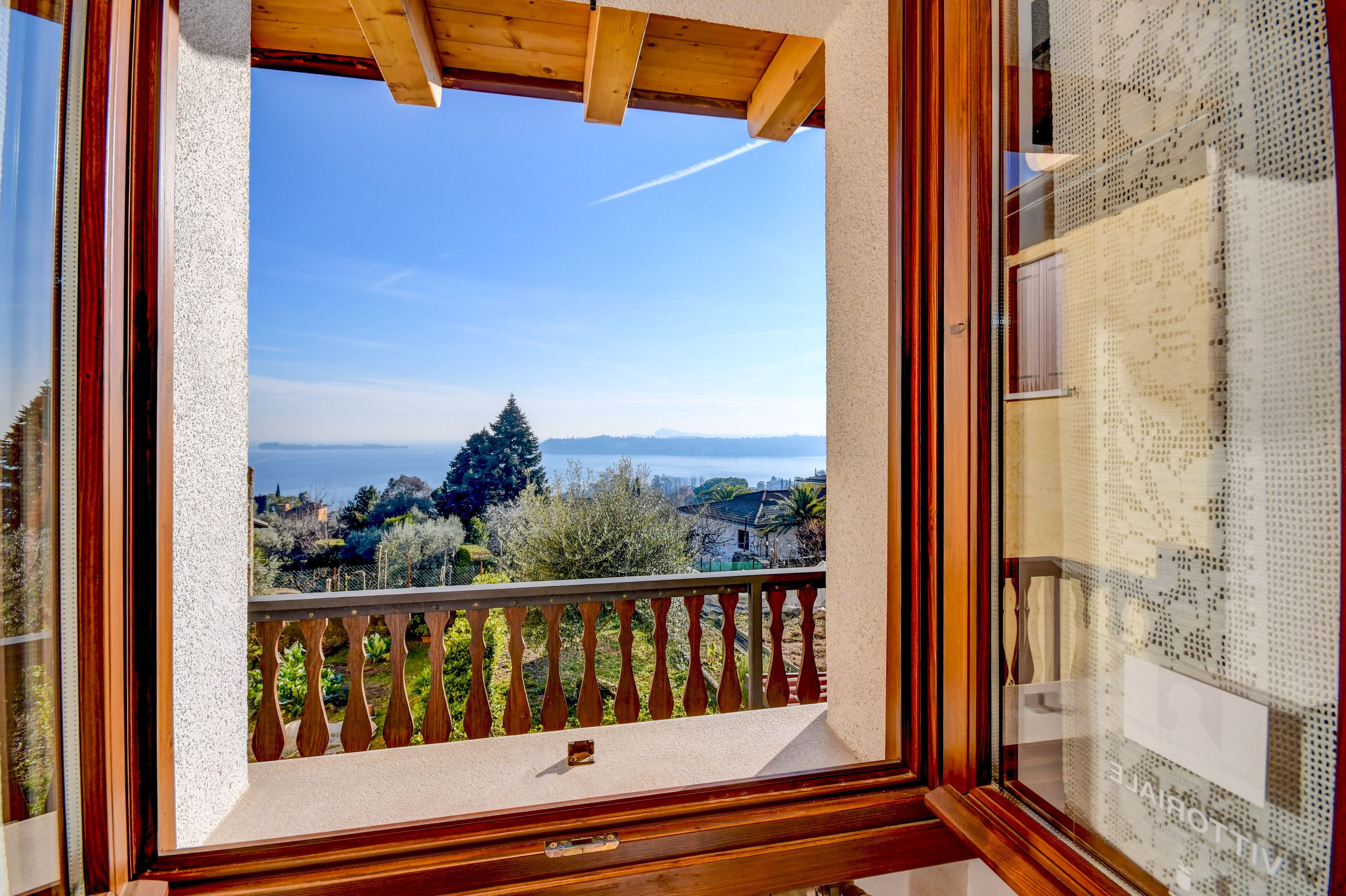 A balcony with a wooden railing, a clear view of a distant tree, and a glimpse of a cityscape in the background.