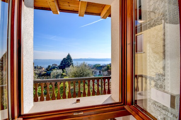 A balcony with a wooden railing, a clear view of a distant tree, and a glimpse of a cityscape in the background.