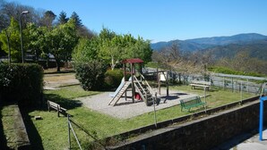 Ein Spielplatz mit Rutsche und Klettergerüsten, umgeben von Bäumen und einer Steinmauer.