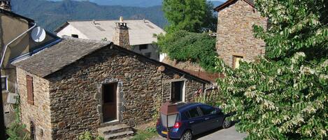 A stone building with a car parked in front, a white car parked in front of the building, and a view of the mountains in the background.