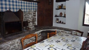 Ein rustikaler Essbereich mit Kamin aus Stein, Holzstühlen und einem Tisch mit floralem Tischlauf.