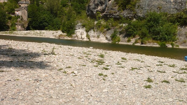 Ein Fluss mit Kiesbett, ein Steinhaus links und ein bewaldeter Hügel.