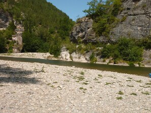 A river with a rocky riverbed, a stone building on the left, and a forested hillside. - Stone house in the heart of the Cévennes, ideal for recharging your batteries (MOISSAC VALLEE FRANCAISE)