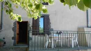 Ein Balkon mit Tisch und Stühlen, eine Steinmauer und eine Tür mit Holzjalousien.