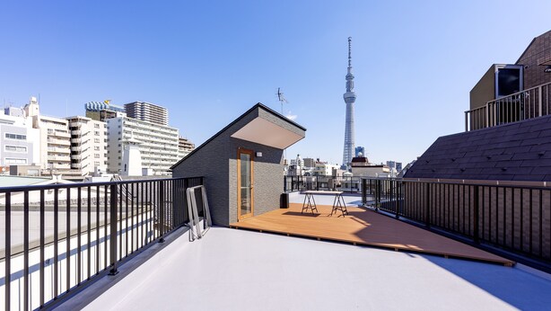 A rooftop terrace with a view of the Tokyo Tower, featuring a small wooden deck and metal railings. - Plat Hostel Keikyu Asakusa Karin (Tokyo)
