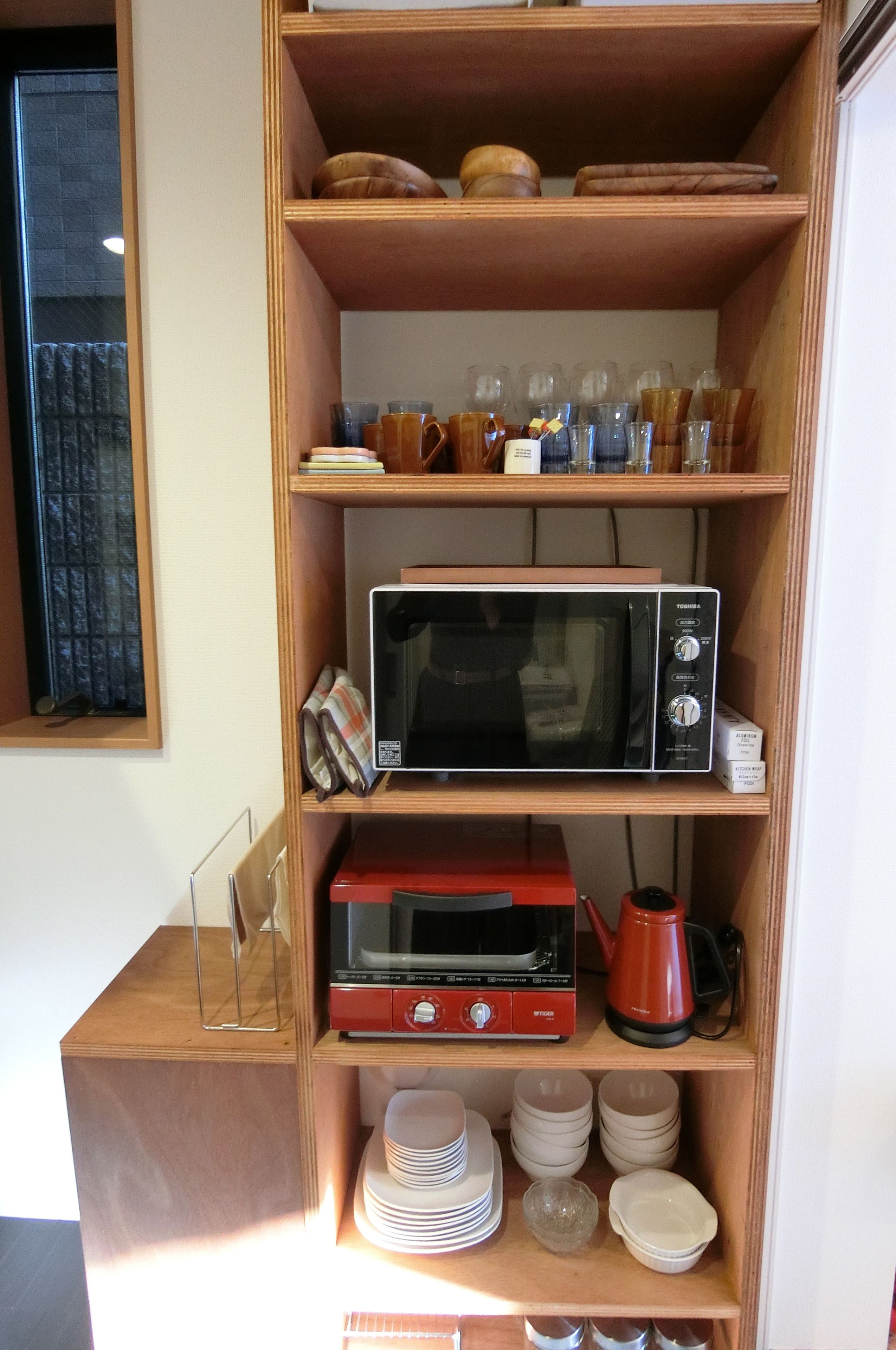 A wooden shelf with kitchen appliances, including a microwave, toaster, and kettle.