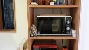 A wooden shelf with kitchen appliances, including a microwave, toaster, and kettle.