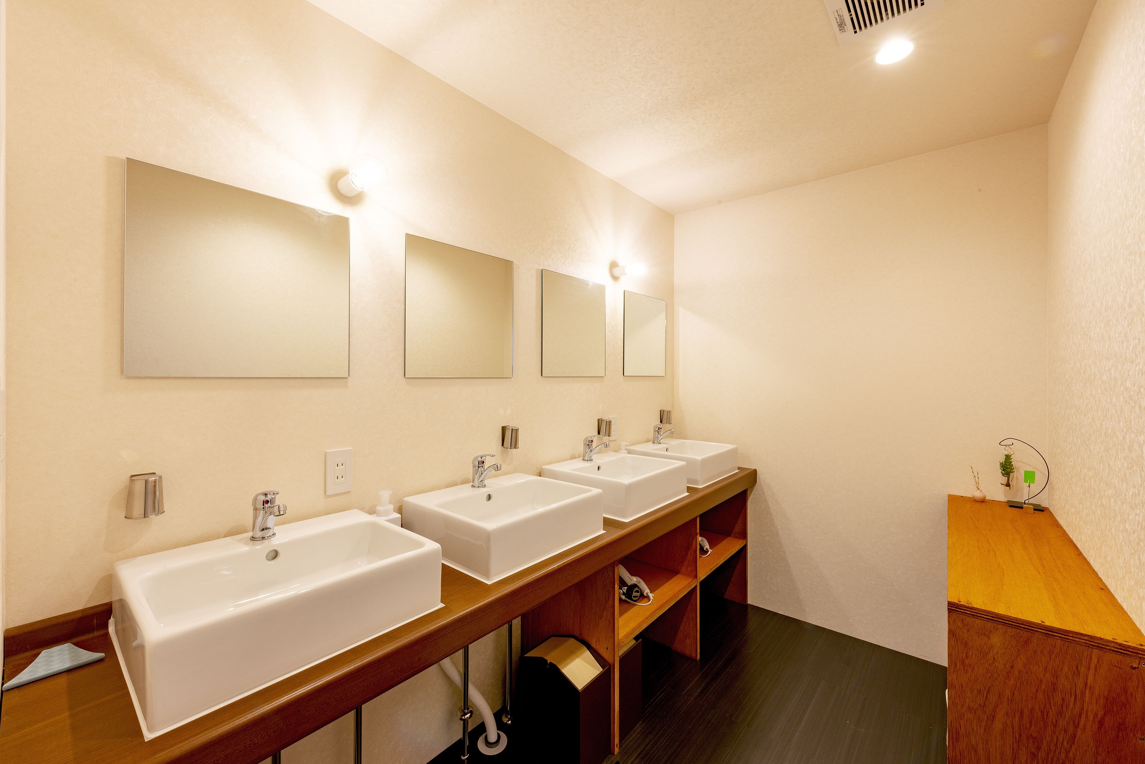 A restroom with three sinks, wooden vanity, and mirrors.