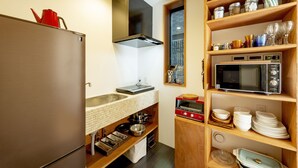 A compact kitchen with a refrigerator, microwave, stove, and various kitchenware on shelves. - Plat Hostel Keikyu Asakusa Karin (Tokyo)
