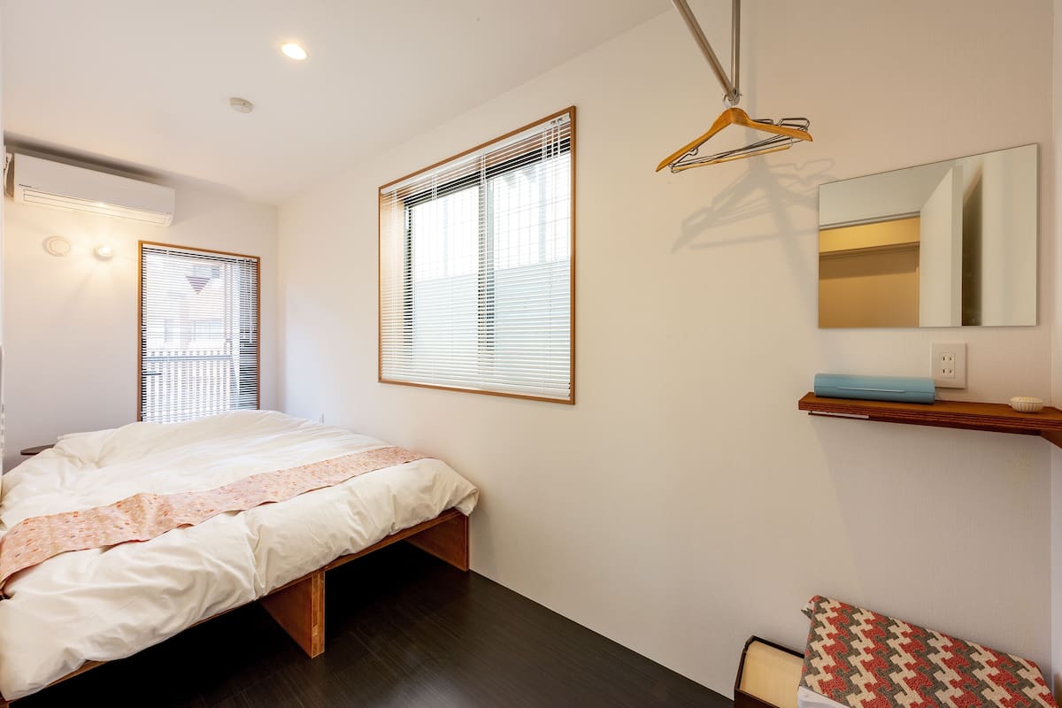 Un dormitorio con cama, mesita de noche, espejo y ventana con persianas.