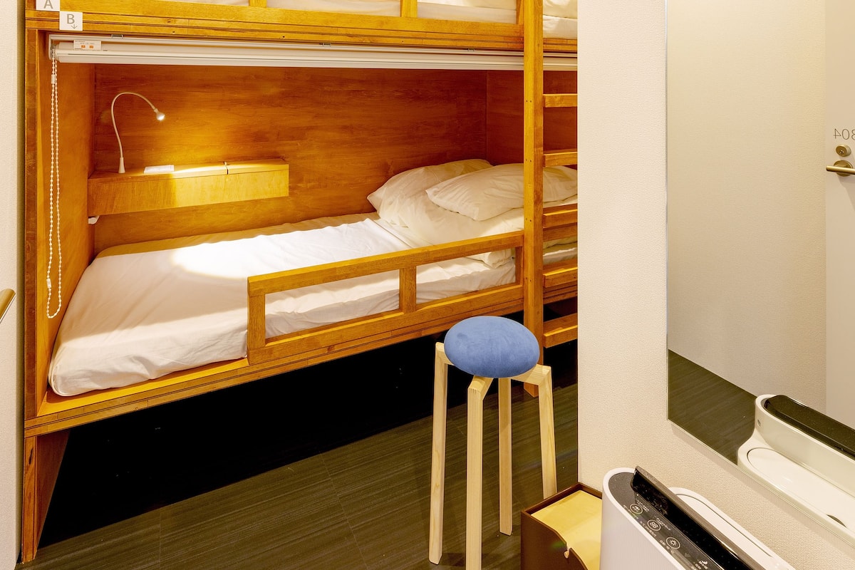 Habitación con literas, cabecera de madera, un taburete pequeño y calefacción integrada.