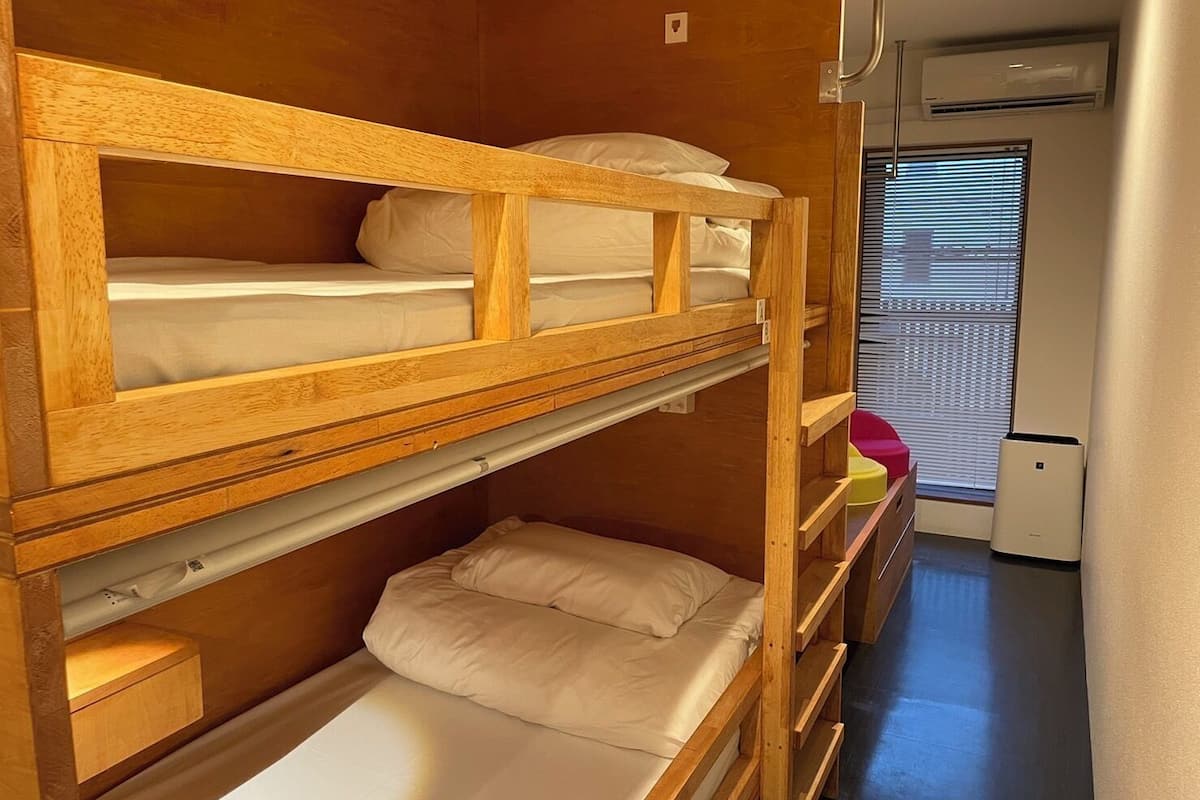 Habitación con literas de madera, ventana con persianas y equipo de aire acondicionado.