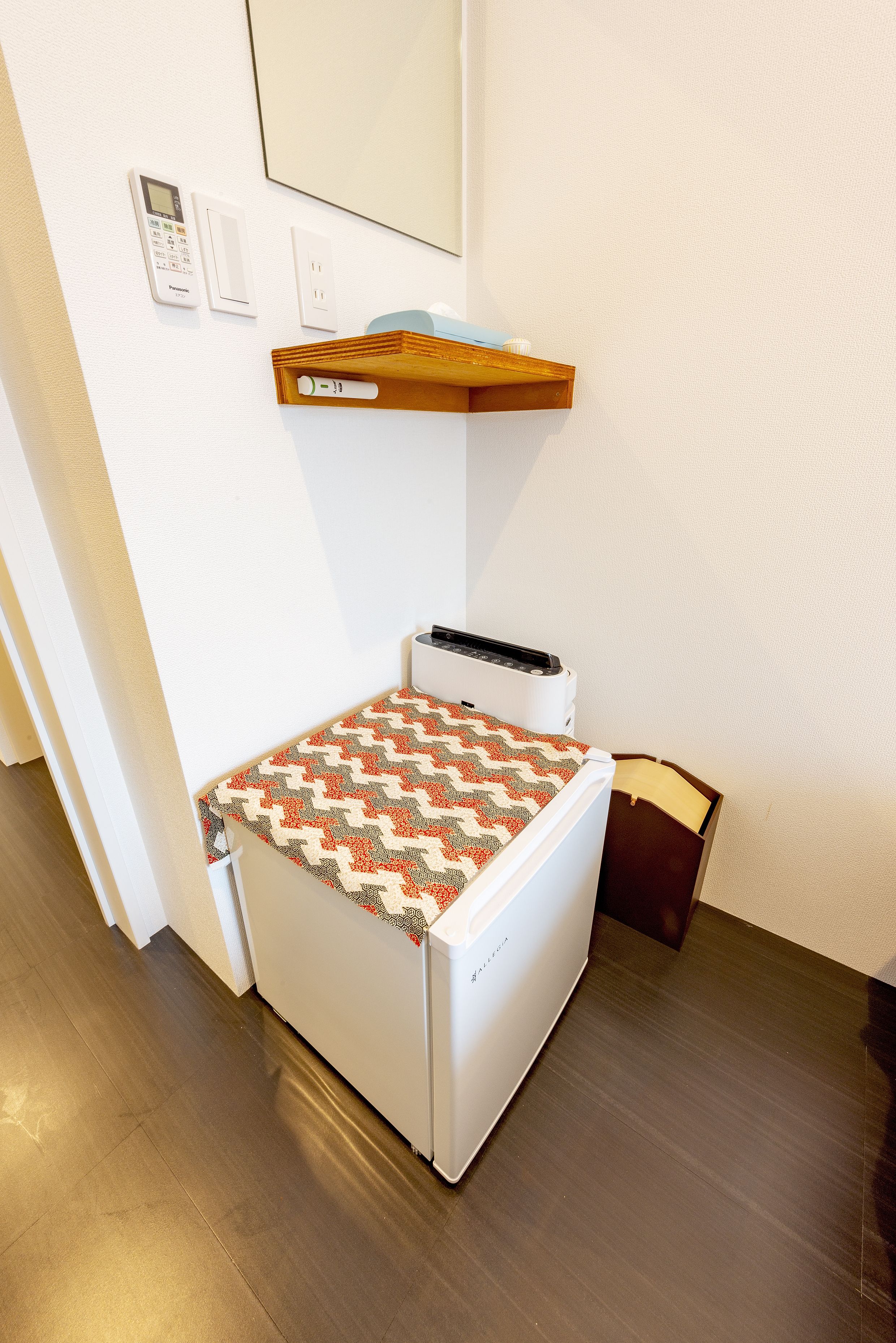 Habitación compacta con lavadora pequeña, un estante de madera encima de la máquina y un enchufe de pared.