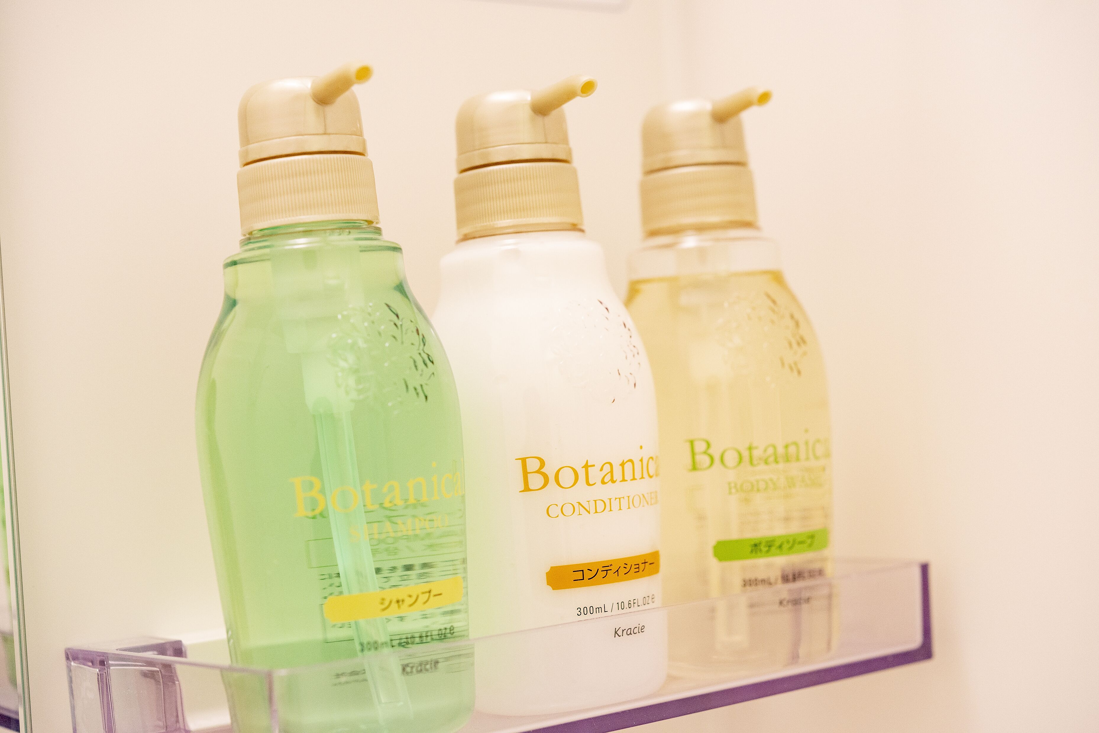 Tres botellas de gel de ducha Botanica sobre una repisa.