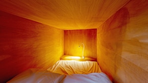 A small, enclosed room with a single bed, a nightstand, and a wall-mounted lamp. - Plat Hostel Keikyu Asakusa Karin (Tokyo)