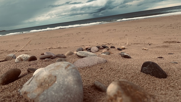 Una playa con una hilera de piedras que conducen al agua, bajo un cielo nublado.