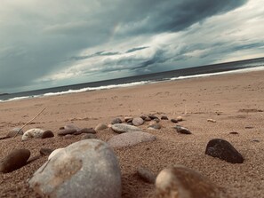 A beach with a line of stones leading to the water, under a cloudy sky.