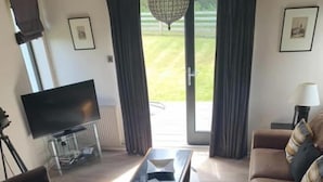 Una sala de estar moderna con sofás de cuero, una mesa de centro de vidrio, un televisor de pantalla plana y un ventanal con cortinas.