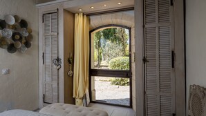A bedroom with a large bed, a window with shutters, and a view of a garden. - LA MAISONNETTE DE ROBINSON HILLSIDE VIEW IDEAL FOR TWO!  (L Isle Sur La Sorgue)