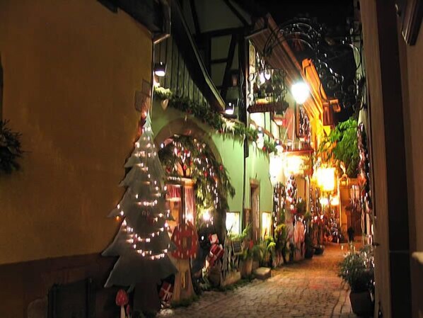 A narrow cobblestone street lined with buildings, decorated with Christmas lights and greenery.