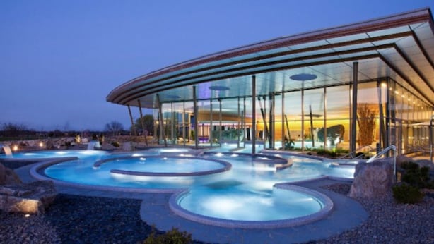 A modern building with a glass facade and a pool area with multiple hot tubs.