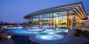 A modern building with a glass facade and a pool area with multiple hot tubs.