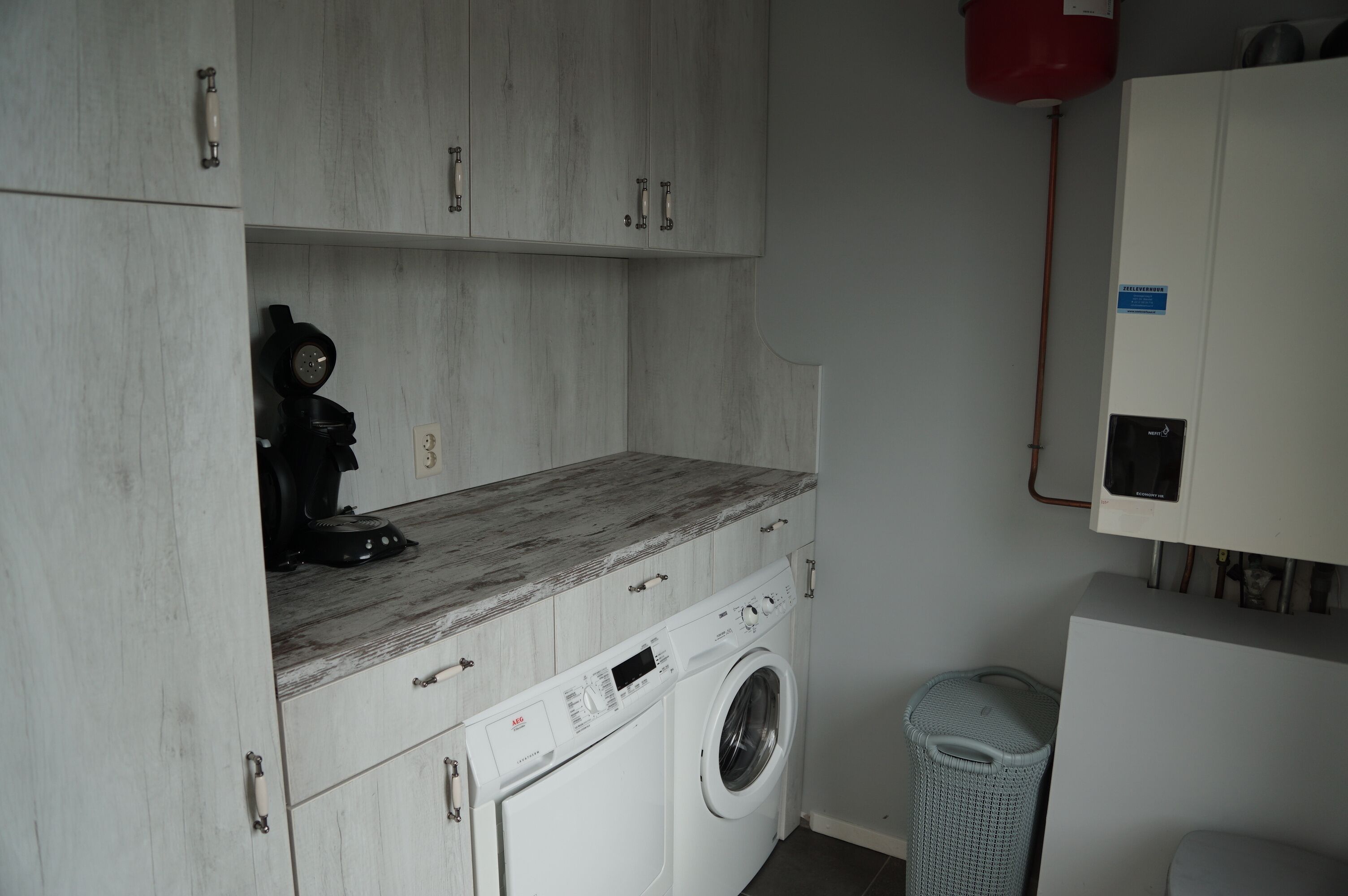 Un espace buanderie comprenant un lave-linge, un sèche-linge et une petite poubelle.