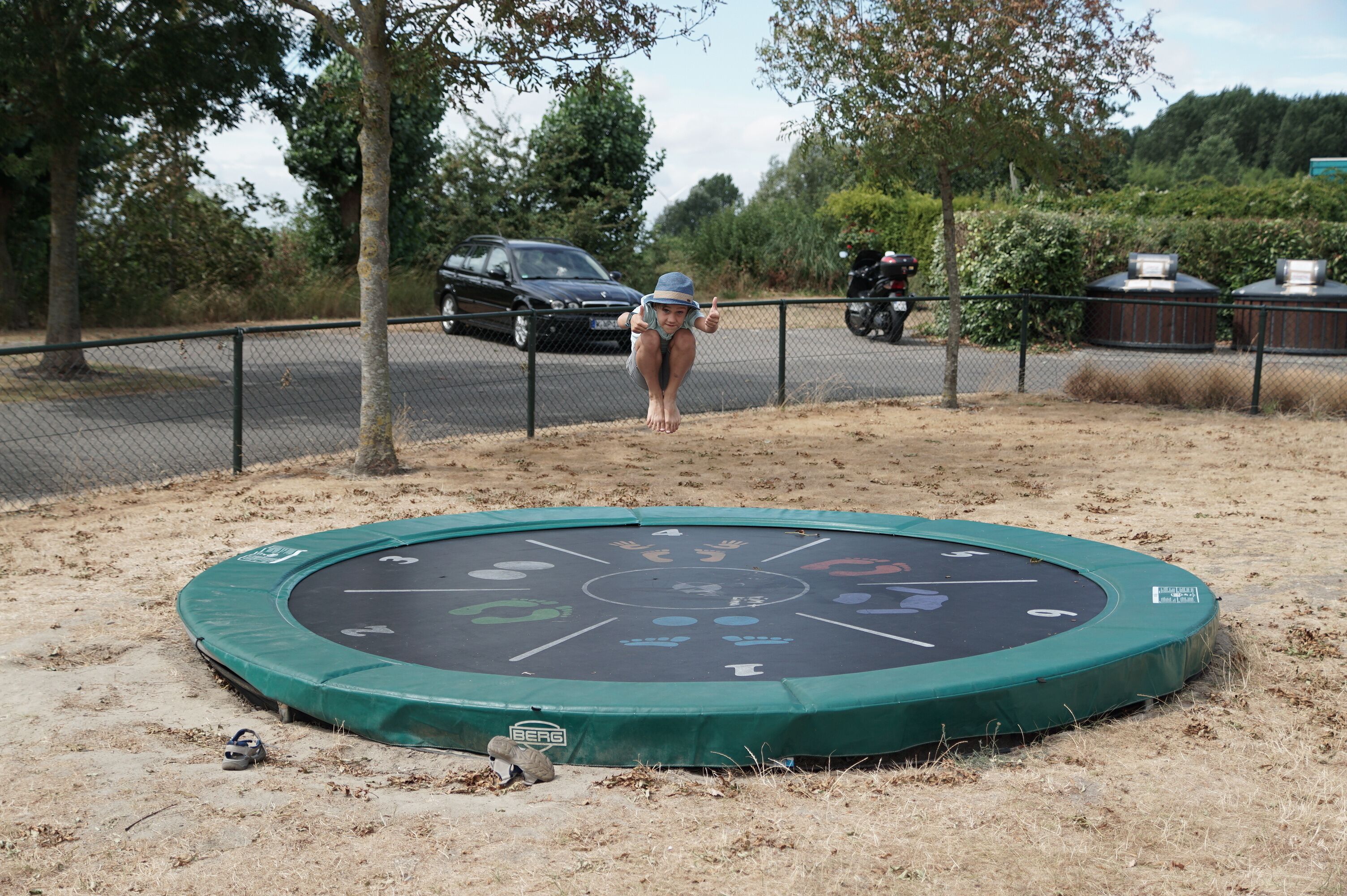 A trampoline with a safety net, surrounded by dry grass and trees.