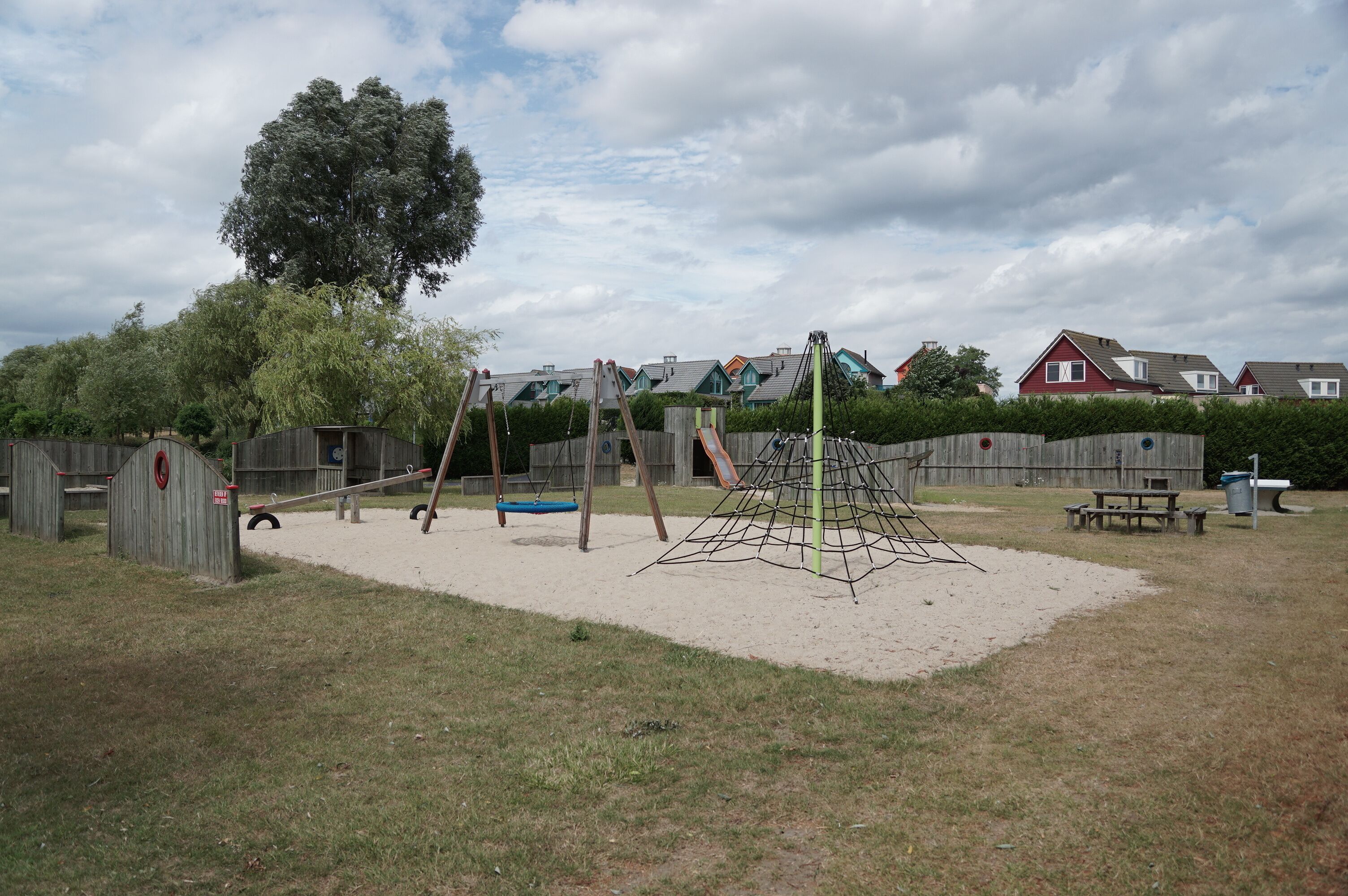 Ein Spielplatz mit Schaukeln, einer Kletterkonstruktion und einem Sandkasten.
