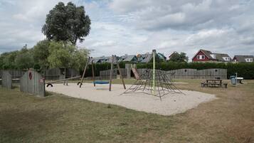 Ein Spielplatz mit Schaukeln, einer Kletterkonstruktion und einem Sandkasten.