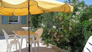 Eine Terrasse mit einem gelben Sonnenschirm, weißen Plastikstühlen und einem Tisch.