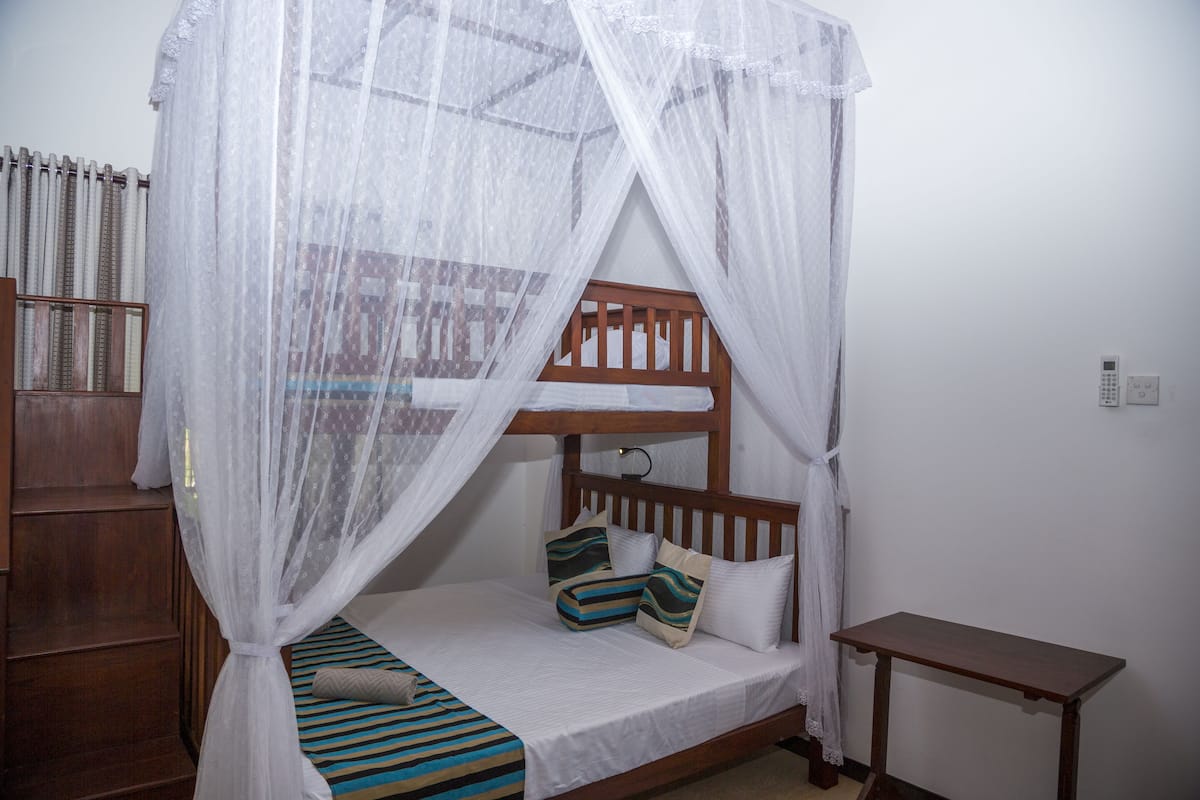 A single bed with a wooden headboard, a bedside table, and a mosquito net.