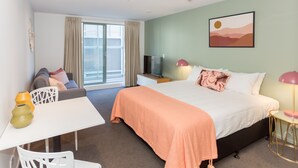 Habitación de hotel con cama, escritorio, silla, televisor y ventana con cortinas.