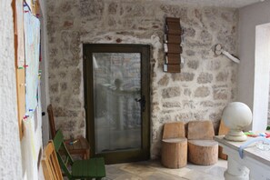Una habitación con pared de piedra, puerta de madera, una silla verde y una mesita con un globo terráqueo.