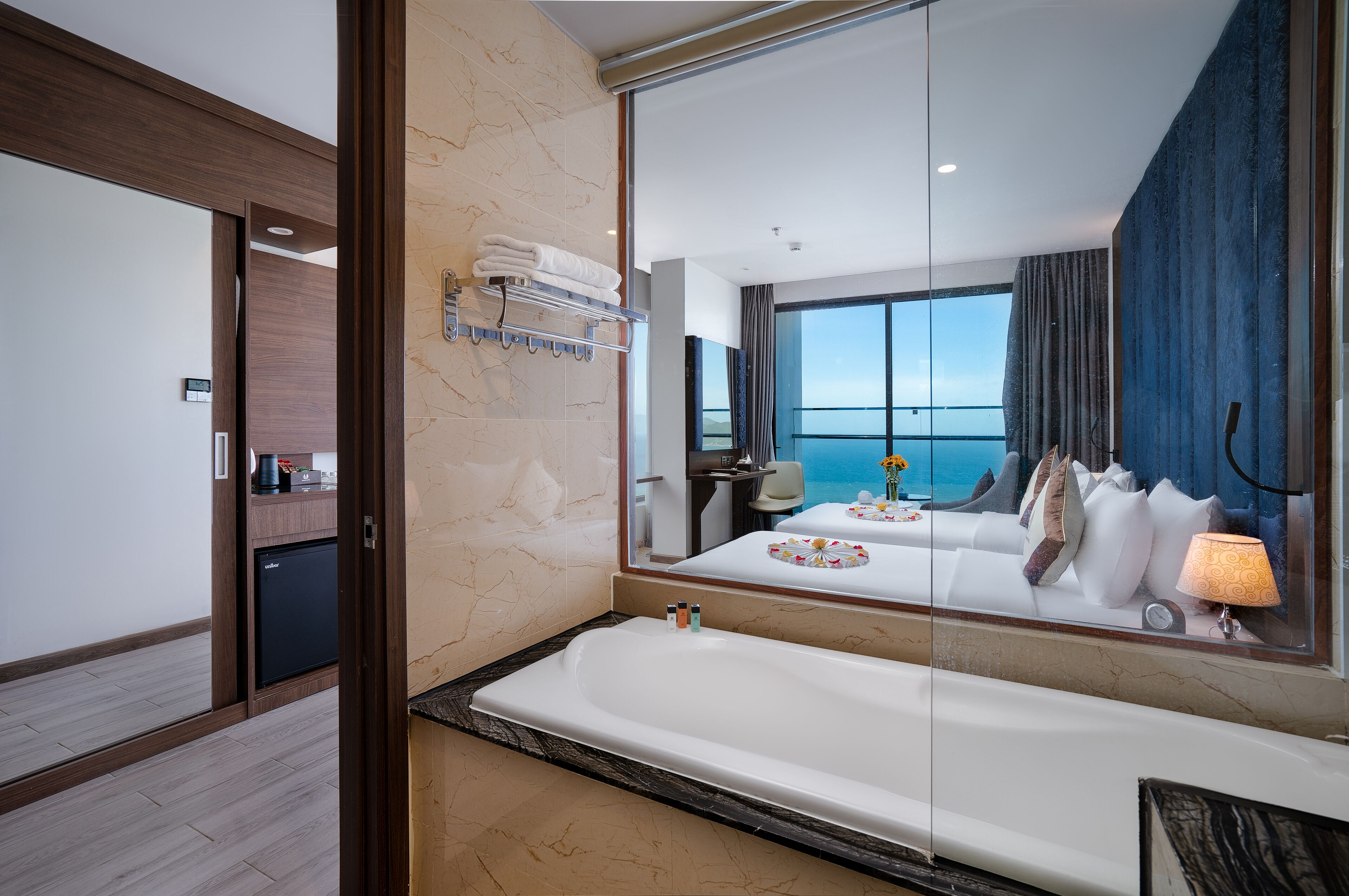 Un baño moderno con un espejo grande, una bañera, un perchero y vistas al mar por la ventana.
