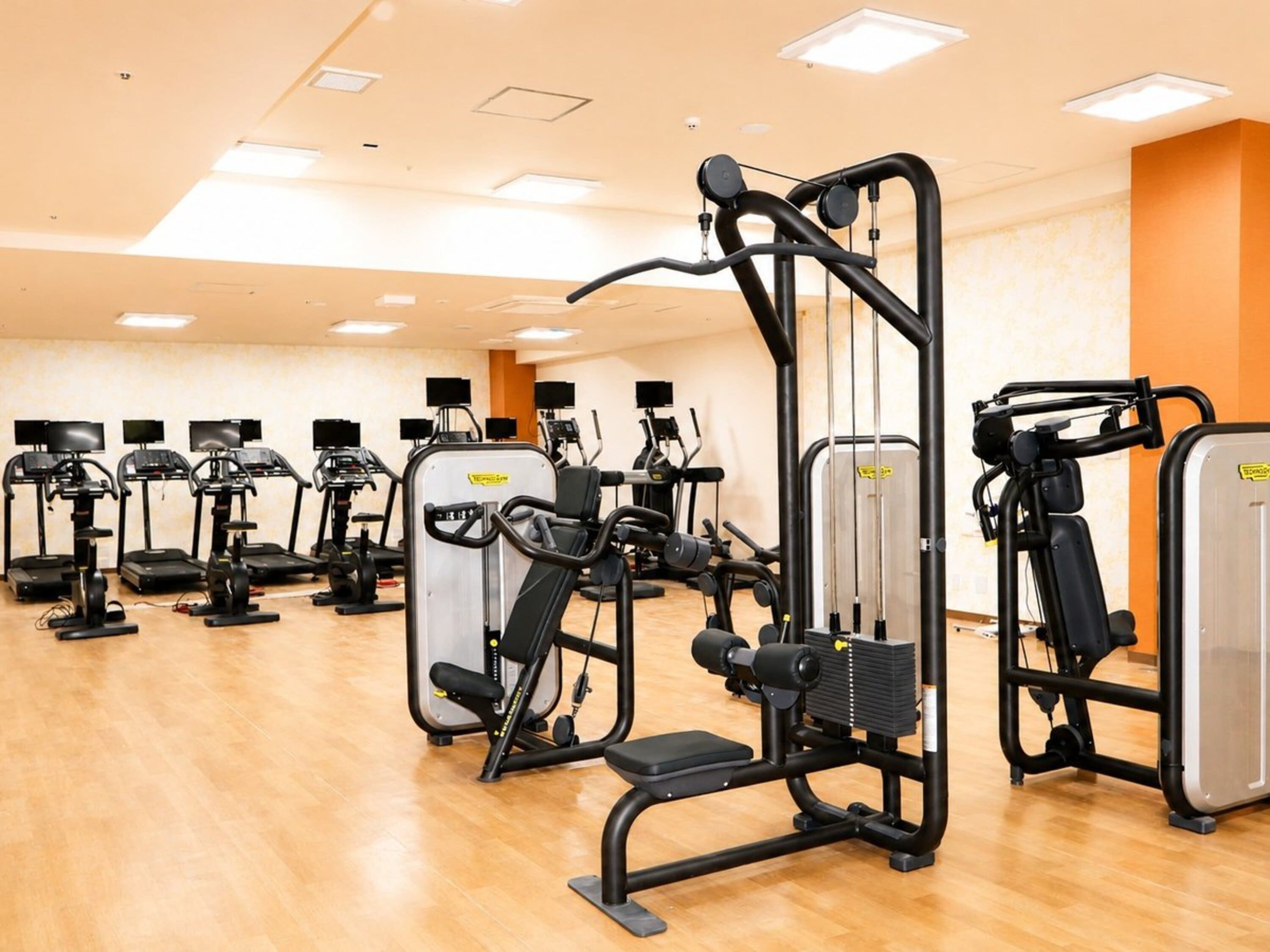 Un gimnasio con diversas máquinas de ejercicio, incluyendo cintas de correr y equipamiento de entrenamiento con pesas, dispuestas en filas.