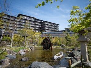 Ein traditionelles japanisches Wasserrad in einem Innenhof, im Hintergrund ein modernes Gebäude.