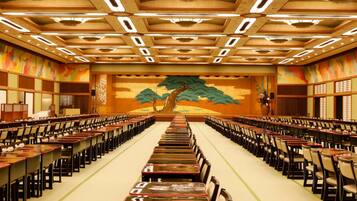 Une salle de conférence avec des rangées de tables et de chaises, une grande fresque sur le mur du fond et un plafond doté d’un éclairage encastré.