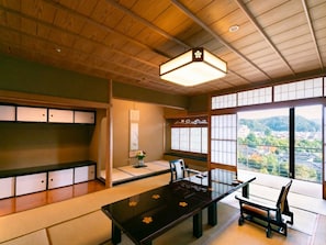 Una habitación japonesa tradicional con suelo de tatami, una mesa baja con superficie negra y vistas a un paisaje montañoso a través de grandes ventanales.