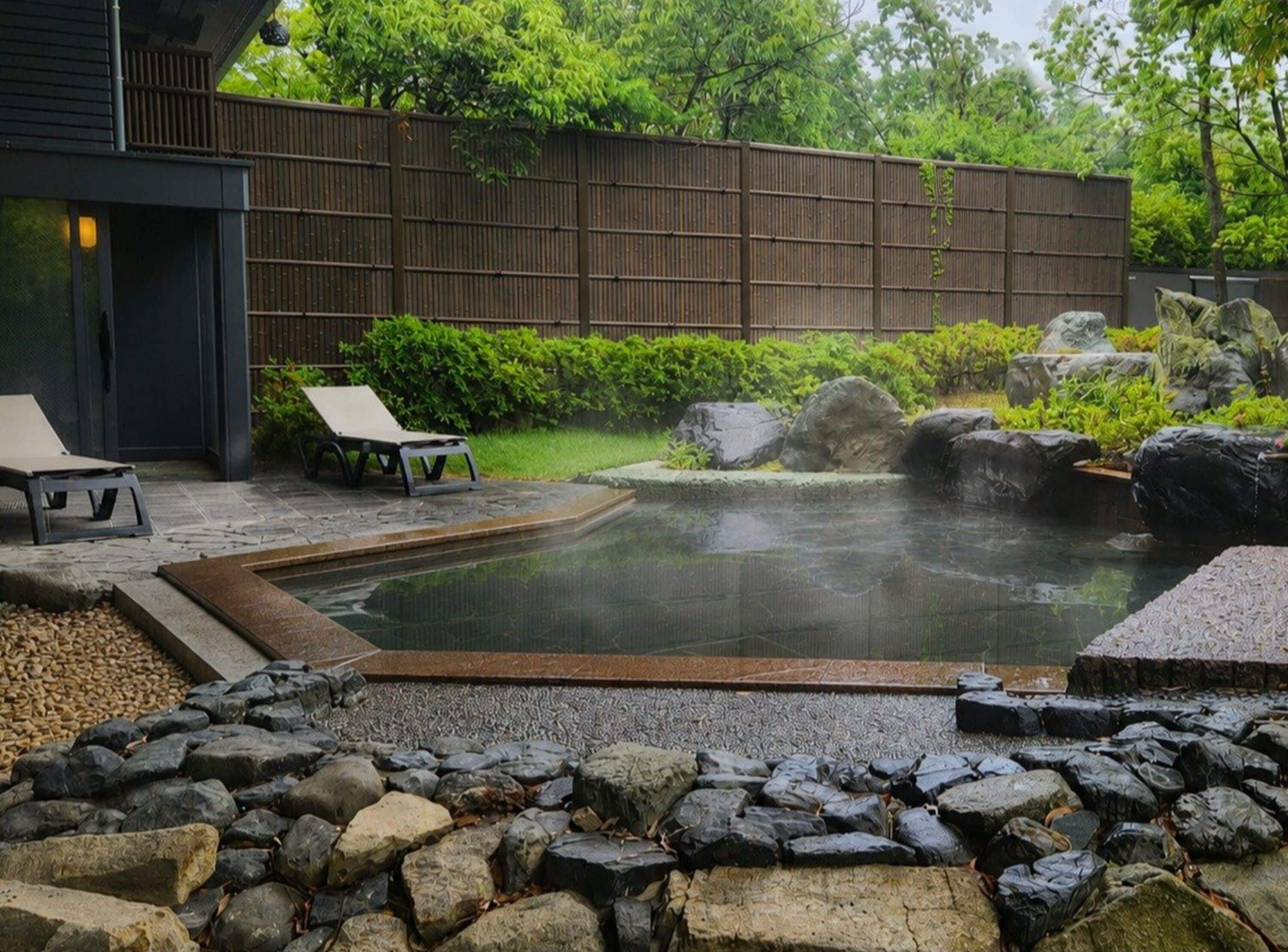 A hot spring area with a stone border, lounge chairs, and a wooden fence.