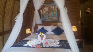 A bed with a canopy, pillows, and a decorative towel arrangement. - The Sandat Bungalow (Penida Island)
