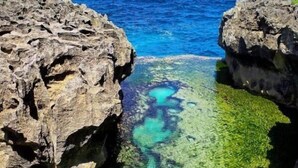 A clear view of a rocky coastline with a narrow water passage between two large rock formations. - The Sandat Bungalow (Penida Island)
